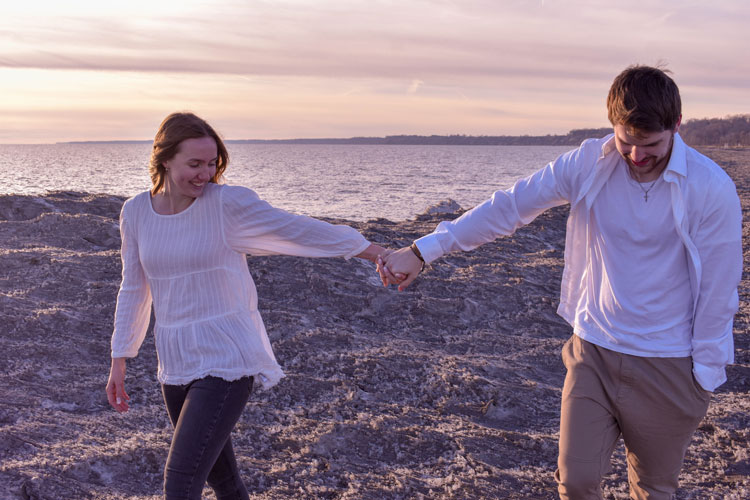 Photos of a newly engaged couple on a beach in winter at sunset wearing all white