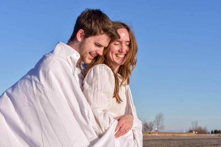 Photos of a newly engaged couple on a beach in winter at sunset wearing all white