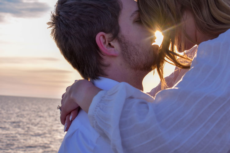 Photos of a newly engaged couple on a beach in winter at sunset wearing all white