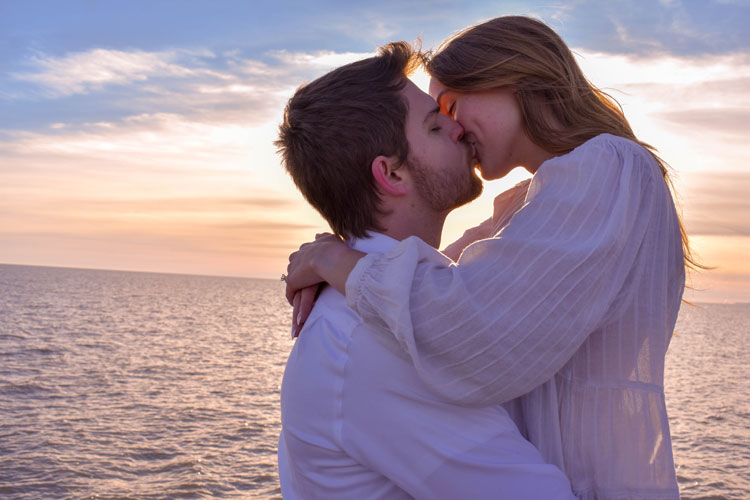 Photos of a newly engaged couple on a beach in winter at sunset wearing all white