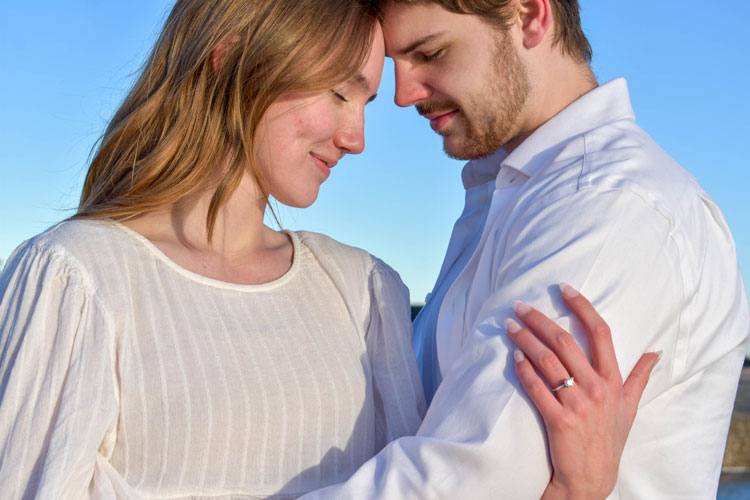 Photos of a newly engaged couple on a beach in winter at sunset wearing all white