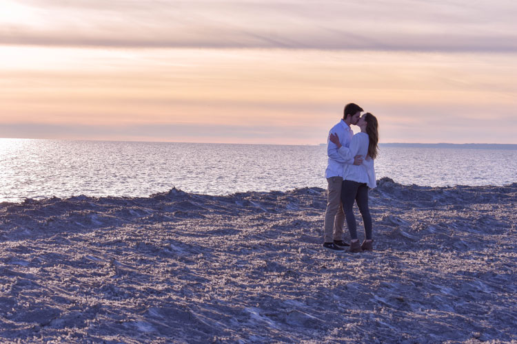 Photos of a newly engaged couple on a beach in winter at sunset wearing all white