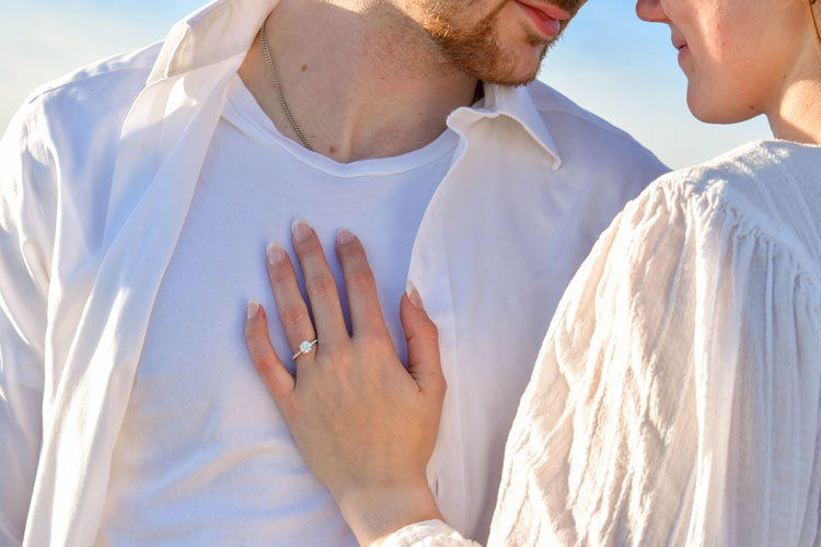 Photos of a newly engaged couple on a beach in winter at sunset wearing all white