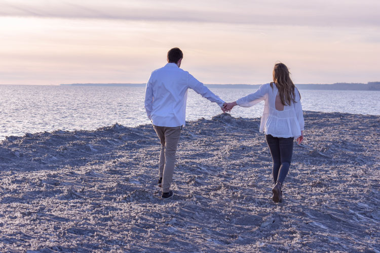 Photos of a newly engaged couple on a beach in winter at sunset wearing all white