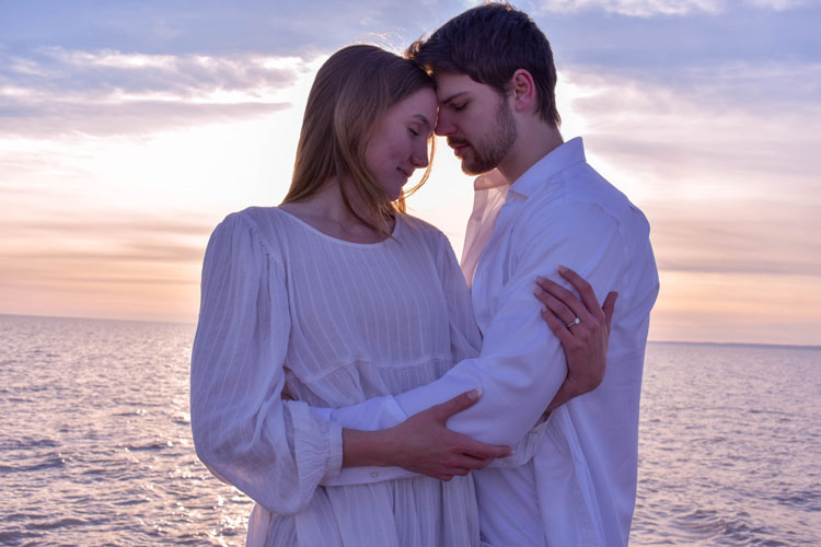 Photos of a newly engaged couple on a beach in winter at sunset wearing all white