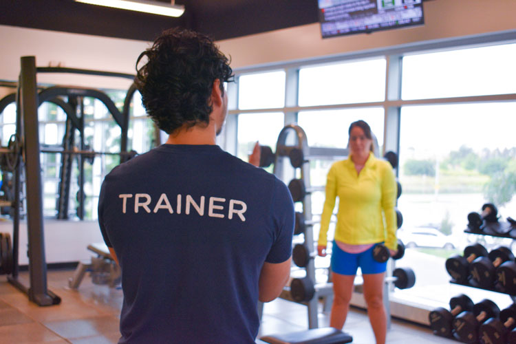 Trainer with shirt that says trainer standing in front of the group he is training at the fitness centre at the Paramount Fine Foods Centre