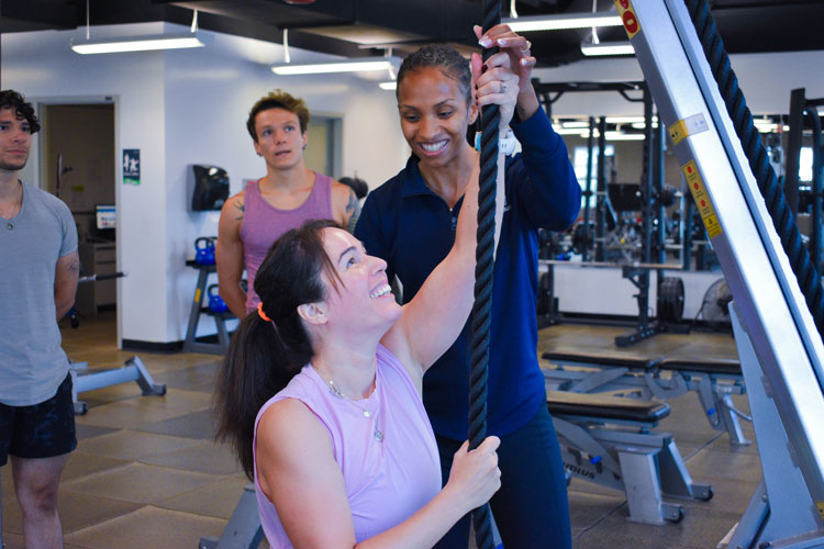 Smiling participant doing a rope pull alongside a trainer at a group fitness class at the fitness centre at the Paramount Fine Foods Centre