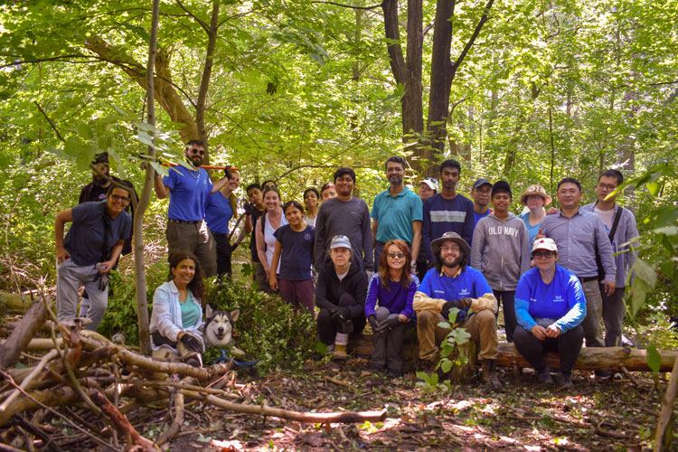 Group of forestry volunteer smiling and posing beside group of pulled groundcovers at the end of an invasive species removal event at Sawmill Valley Trail 