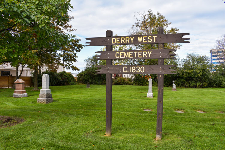 Sign at Derry West Cemetery that reads DERRY WEST CEMETERY C. 1830 with headstones in behind